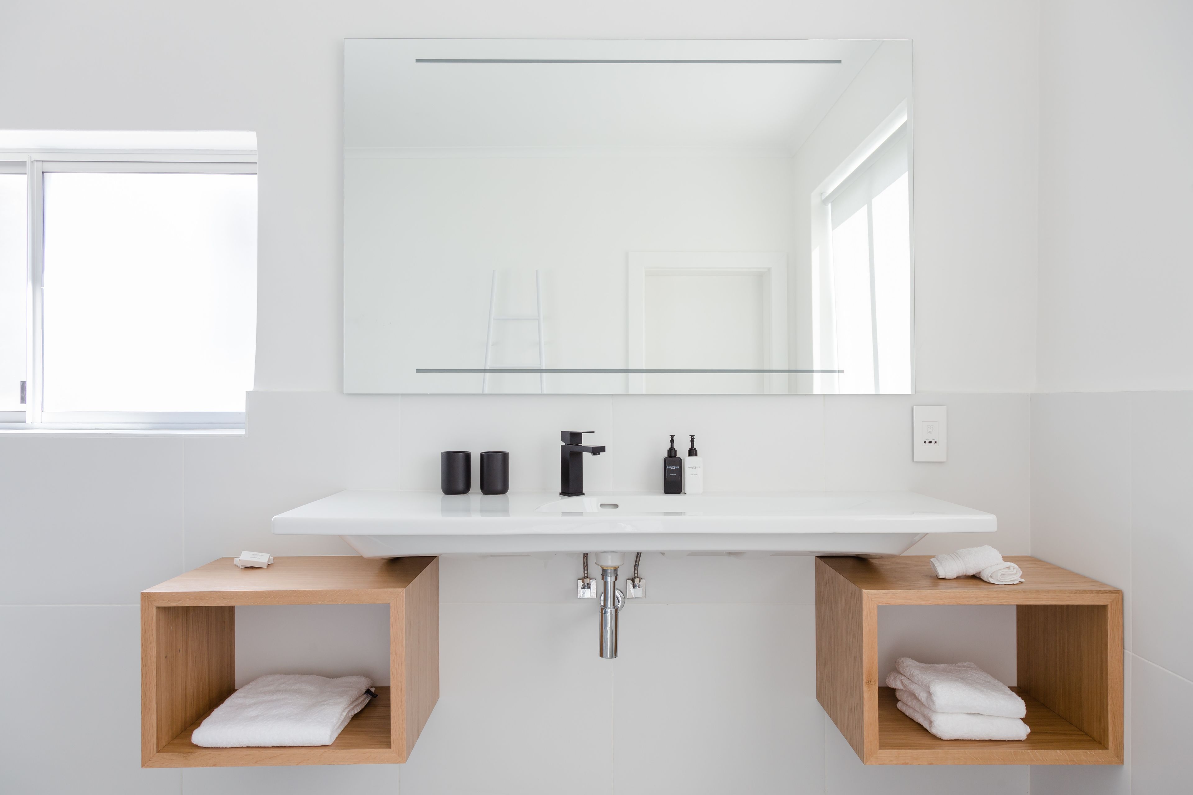 A modern bathroom with a white sink, black faucet, and two wooden towel racks.