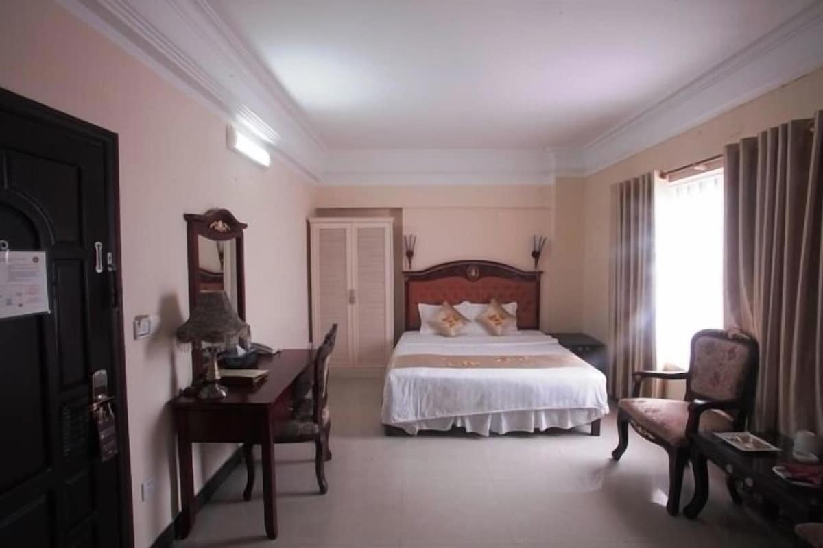 A hotel room with a bed, a desk, a chair, a wardrobe, and a window with curtains.