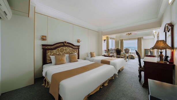 Quarto de hotel com duas camas, uma mesa, uma cadeira e vista para o mar.