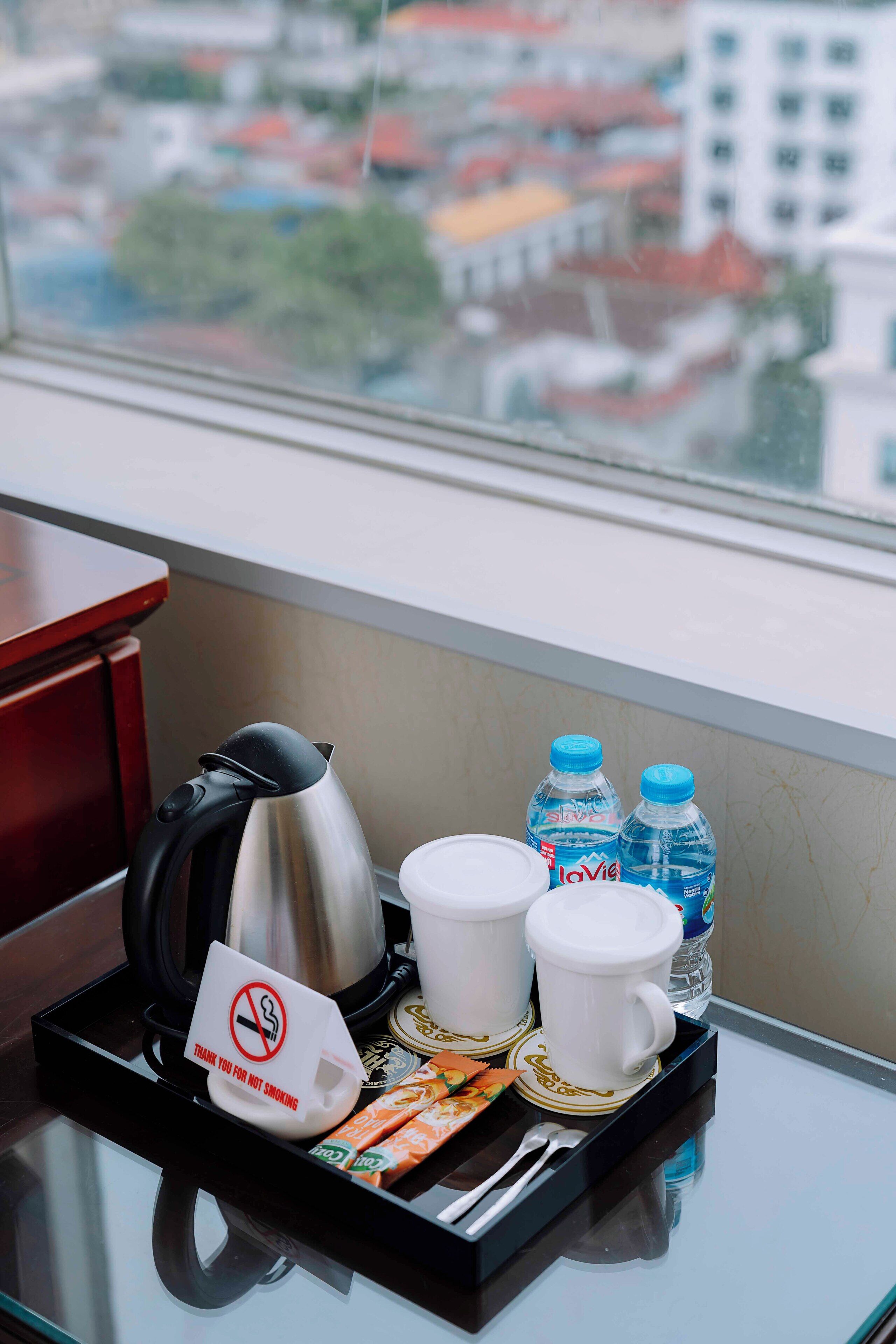 Een dienblad met een waterkoker, twee bekers, twee waterflessen, een dienblad met een rookvrij sign, en een dienblad met snacks en een lepel.