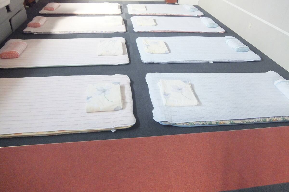 A room with multiple beds arranged in rows, each with a pillow and a blanket.