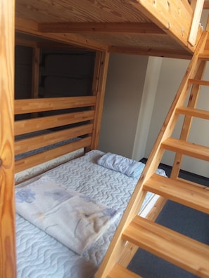 Een houten stapelbed met een ladder, een matras met een gestreept hoesje en een hoofdbord.