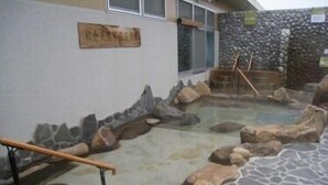 Un sendero de piedra que conduce a un área de aguas termales, con baranda de madera y pared de piedra con una placa.