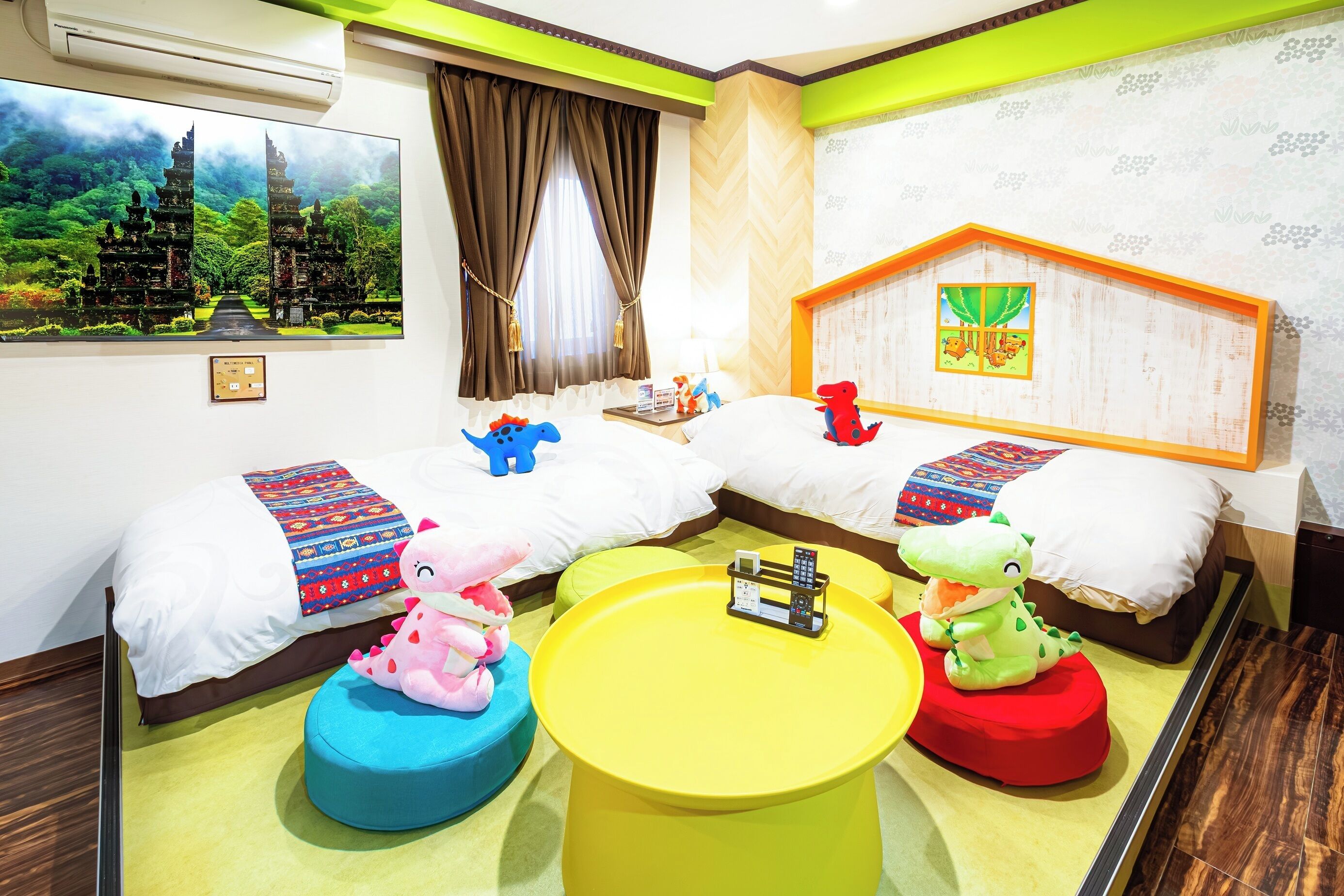 A hotel room with two beds, a large window with curtains, a wall-mounted TV, and a colorful mural.