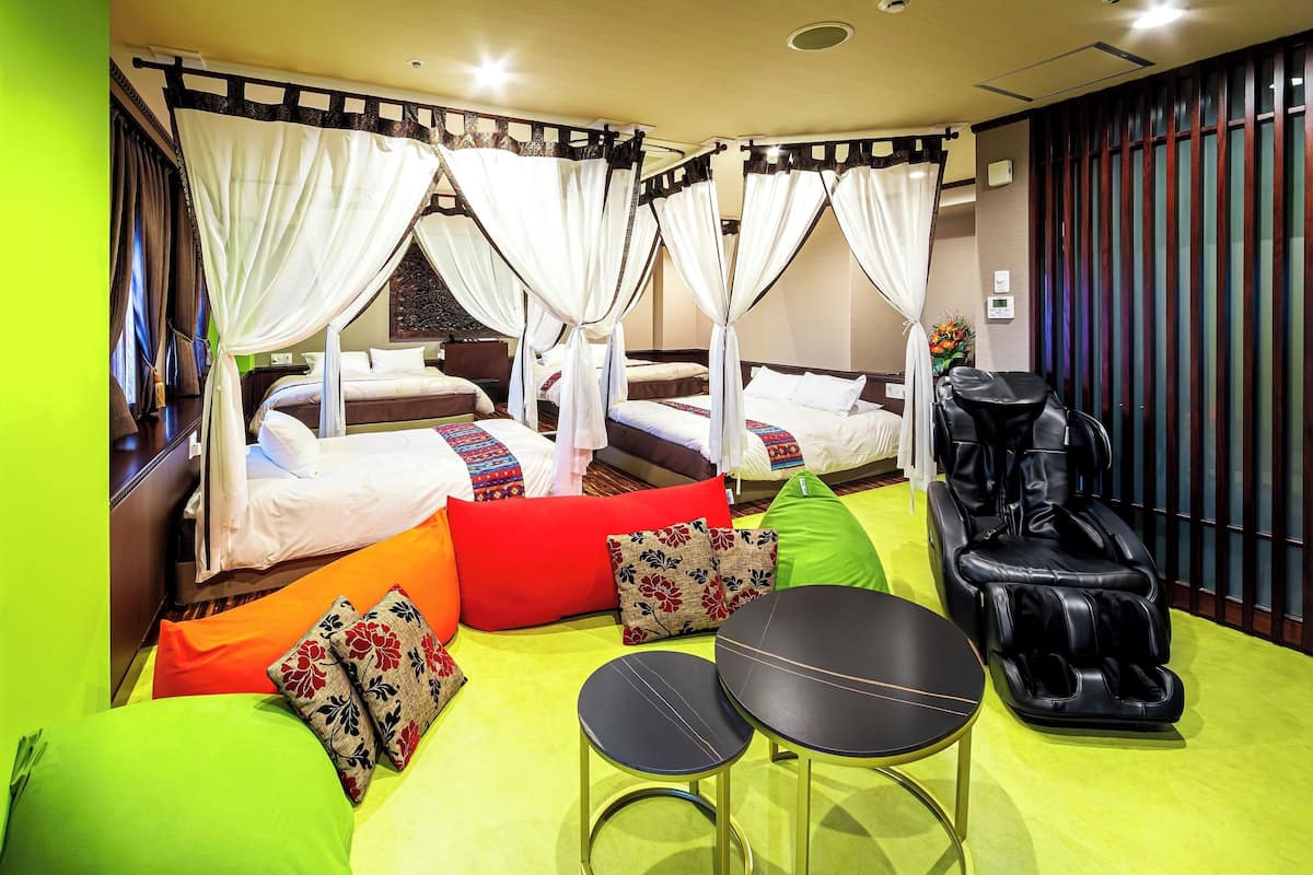 Een hotelkamer met vier bedden, een massagestoel, twee kleine tafels en kleurrijke kussens.