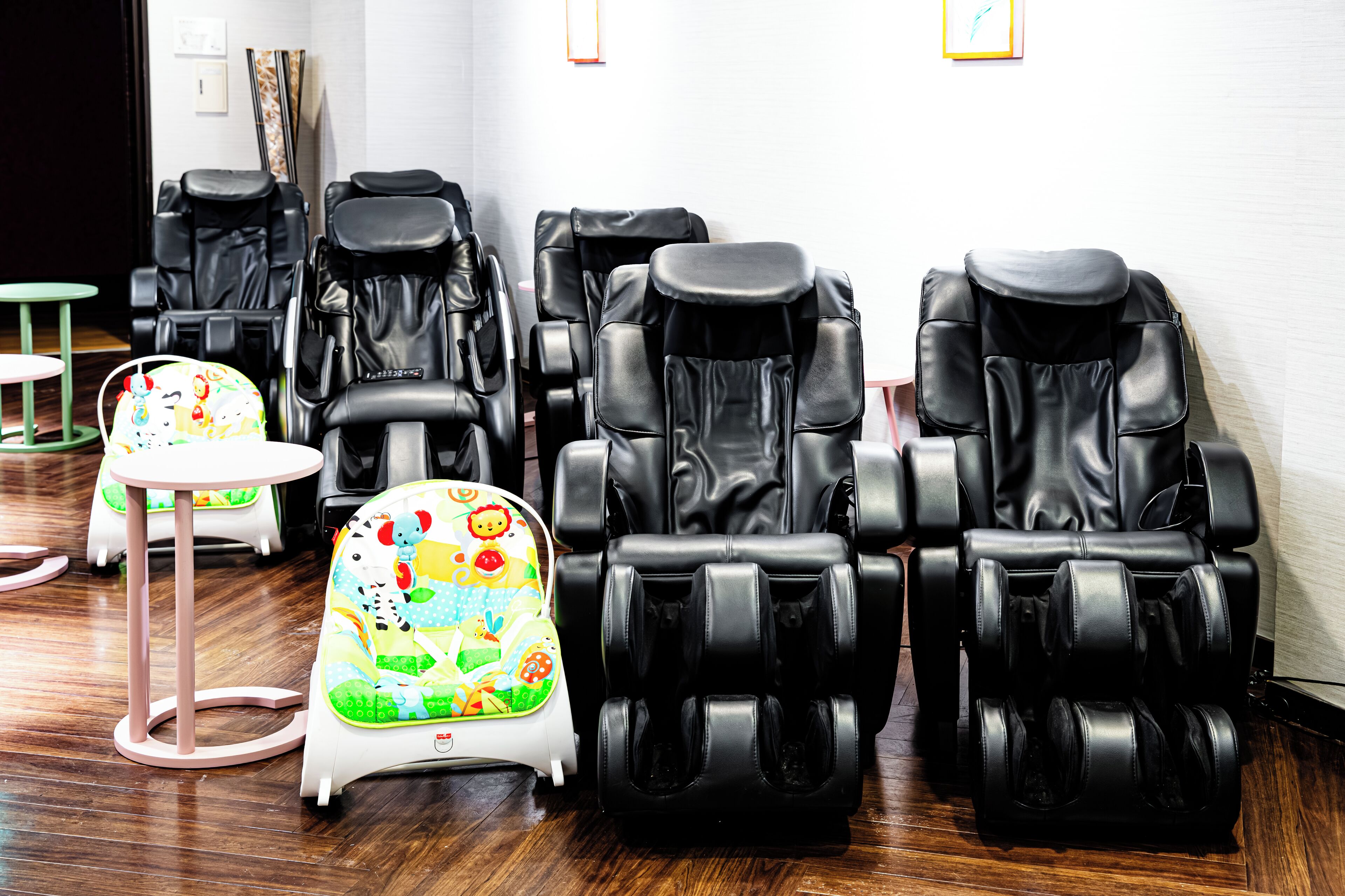 Una habitación con varias sillas de masaje, una mesita pequeña y un sillón infantil de colores.
