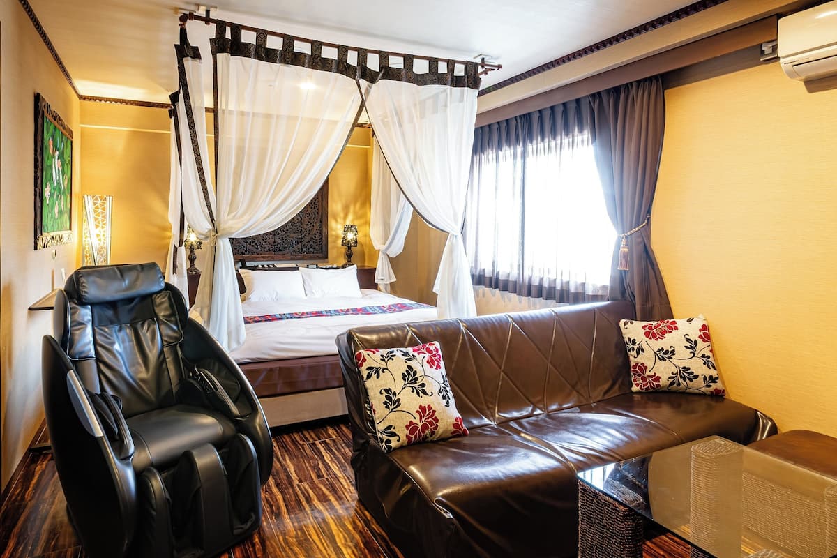 Een slaapkamer met een hemelbed, een massagestoel, een leren bank en een kleine tafel.