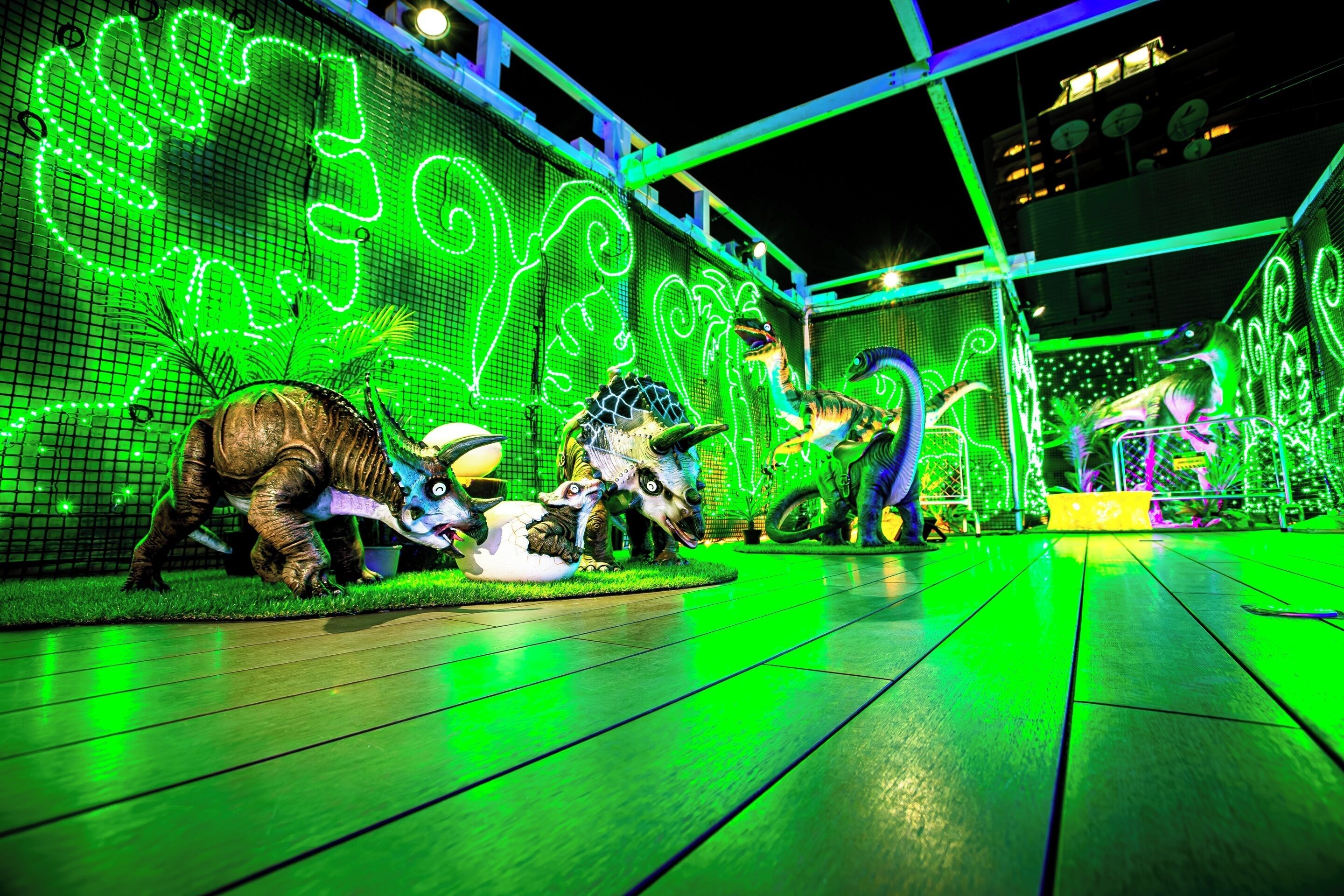 Une exposition sur le thème des dinosaures, avec un décor illuminé de lumière verte et un plancher en bois.