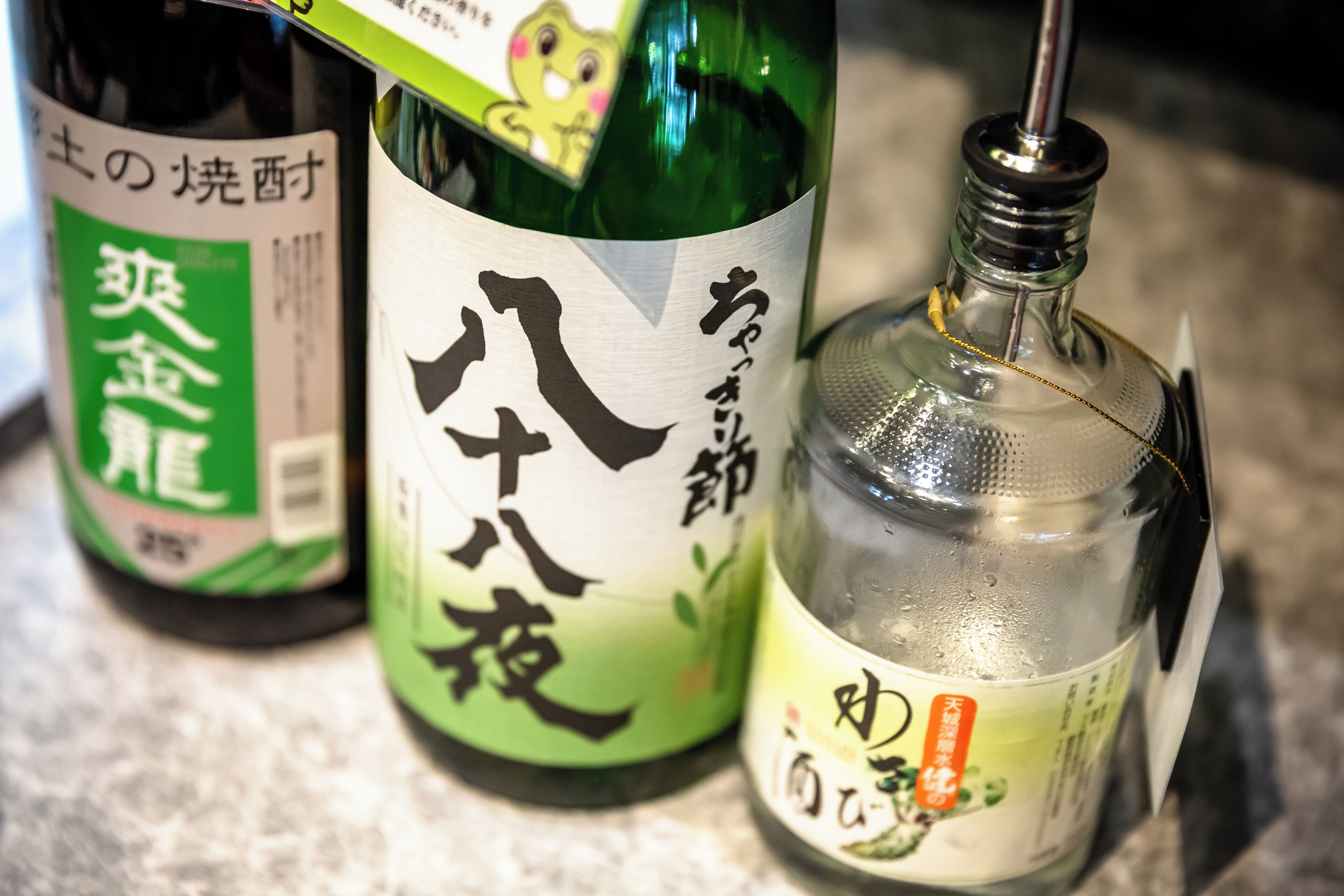 Three bottles of Japanese sake on a countertop.