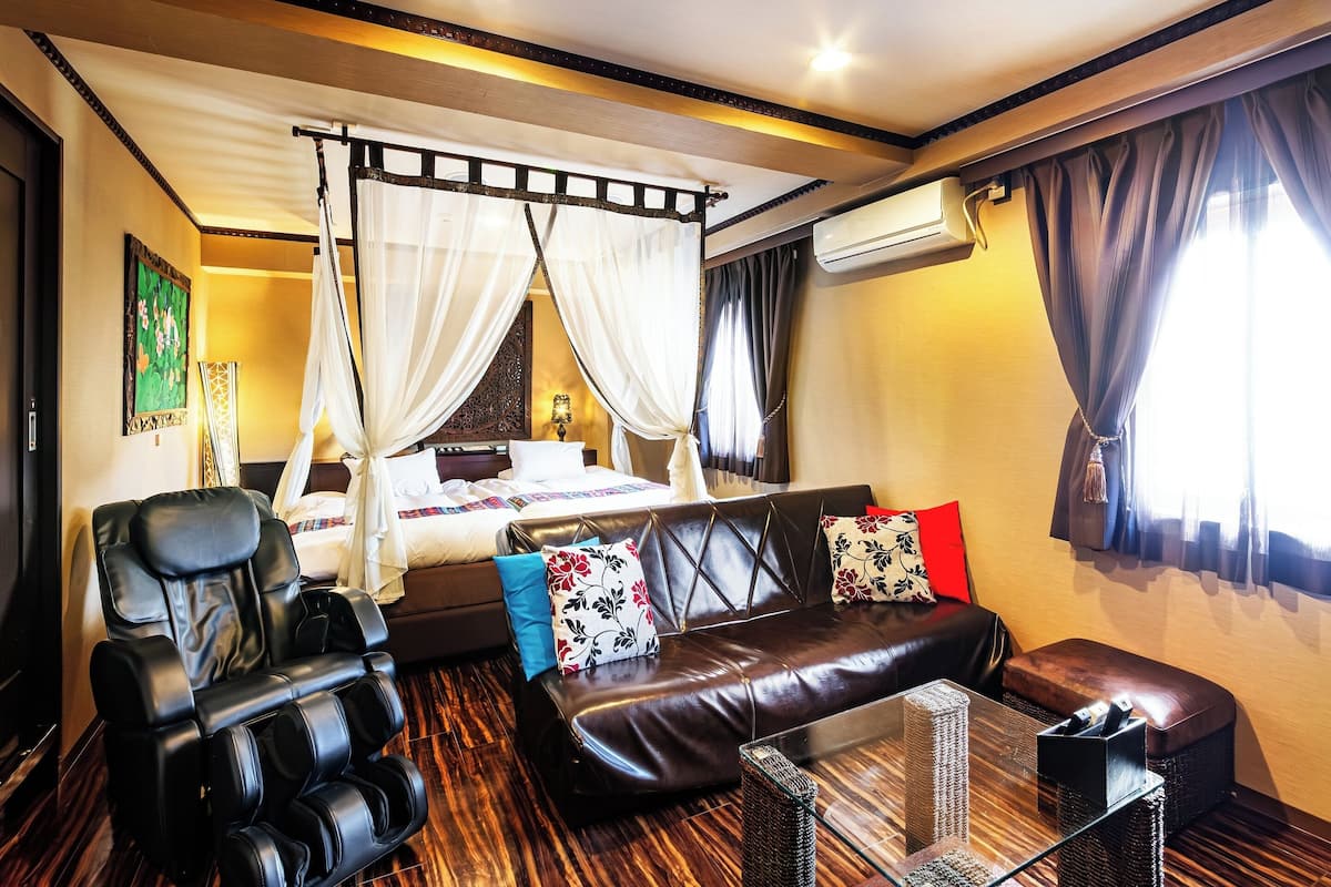 Een kamer met een bed, massagestoel, bank en een glazen tafel.