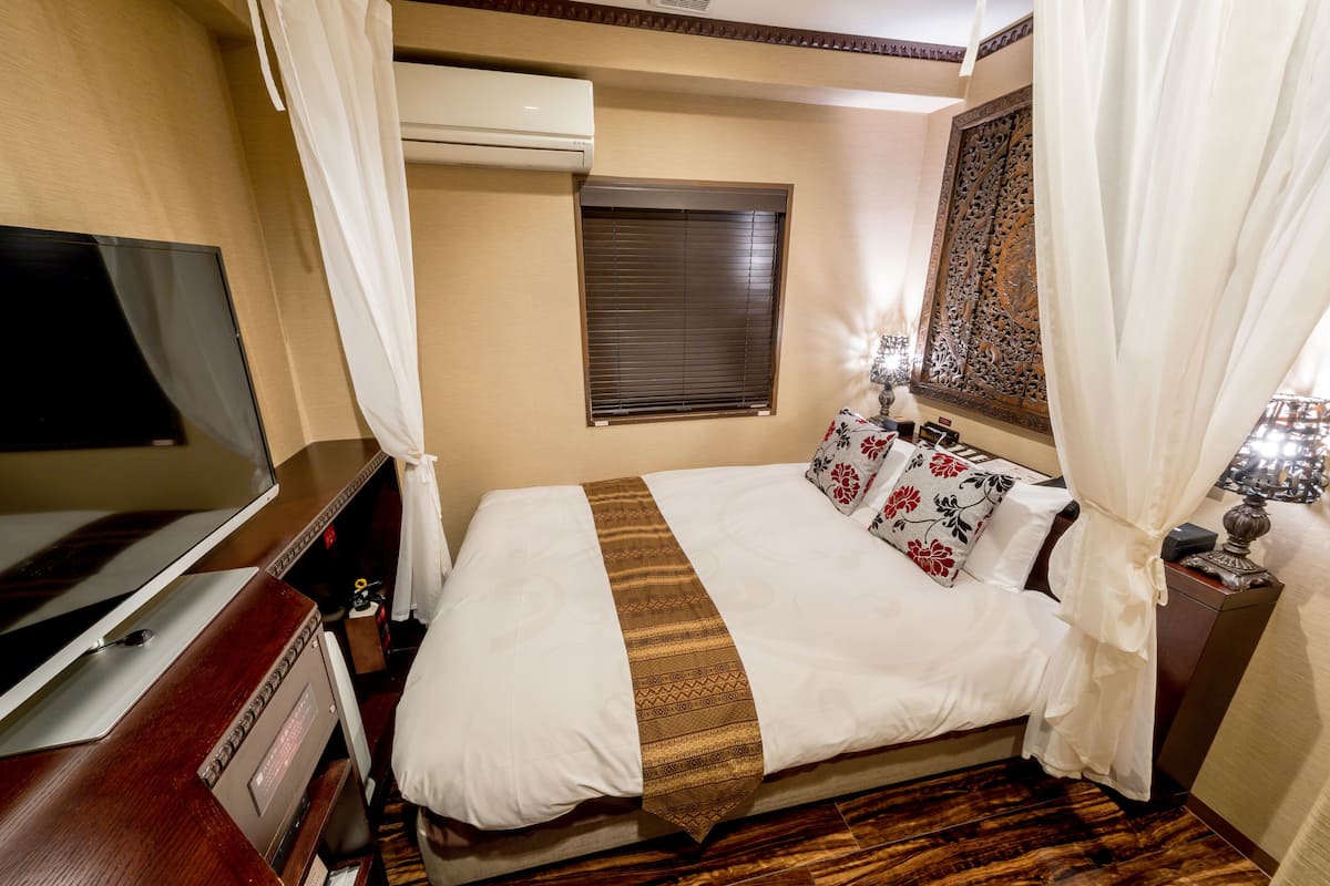 Een hotelkamer met een bed, een televisie, een raam met zonwering en een decoratief wandobject.