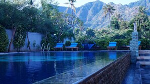A swimming pool with blue lounge chairs and a stone wall. - Antari Hotel (Pemuteran)