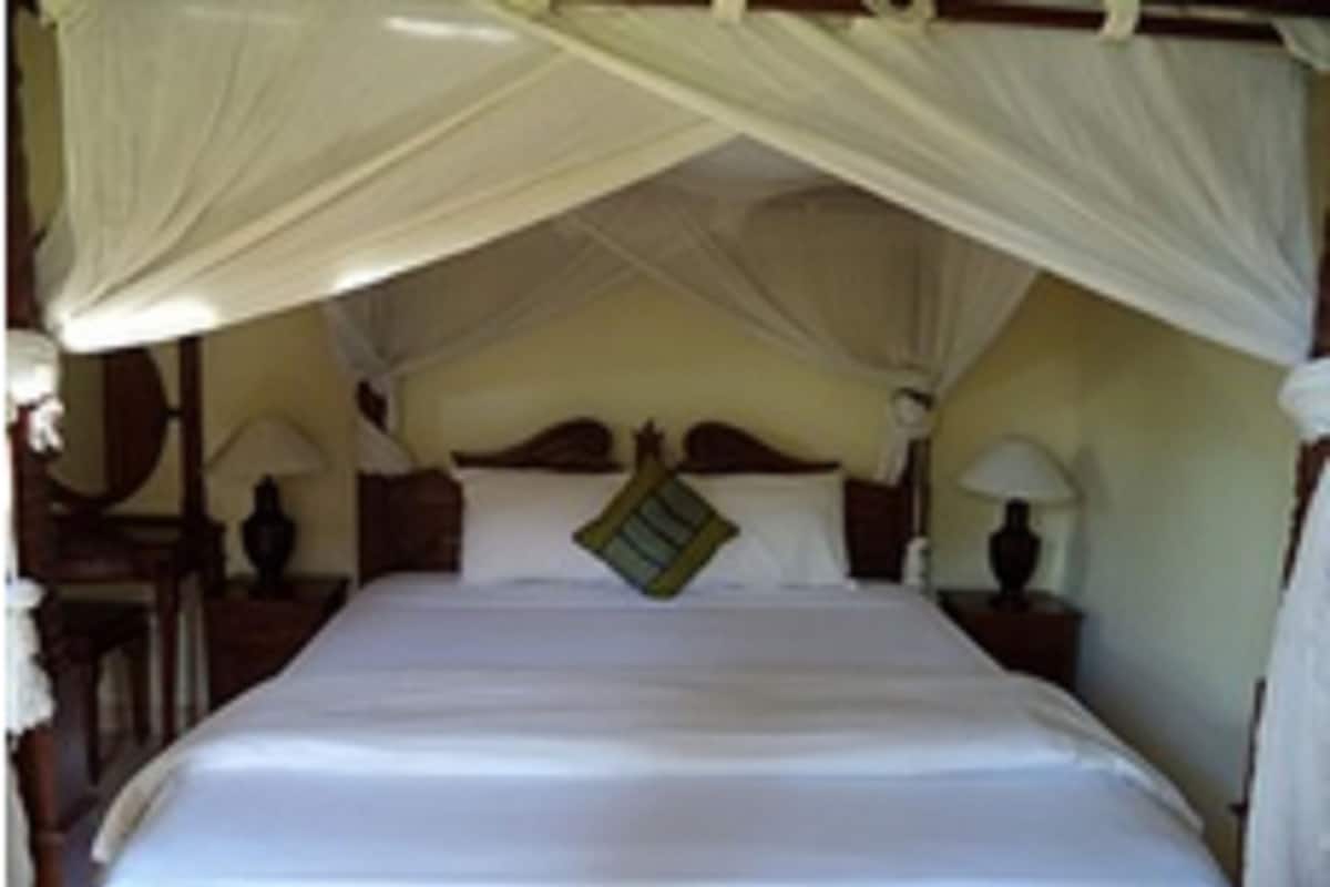 Een bed met hemelbed, houten hoofdbord en twee nachtkastjes met lampen.