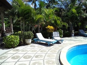 A pool area with tiled flooring, two lounge chairs, and various tropical plants. - Coral Bay Bungalow (Karangasem)