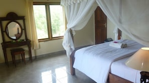 A bedroom with a bed, a nightstand, a mirror, and a window with curtains. - Coral Bay Bungalow (Karangasem)