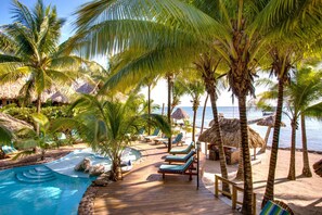 A tropical resort with a wooden deck, lounge chairs, a pool, and palm trees. - Xanadu Island Resort (San Pedro)