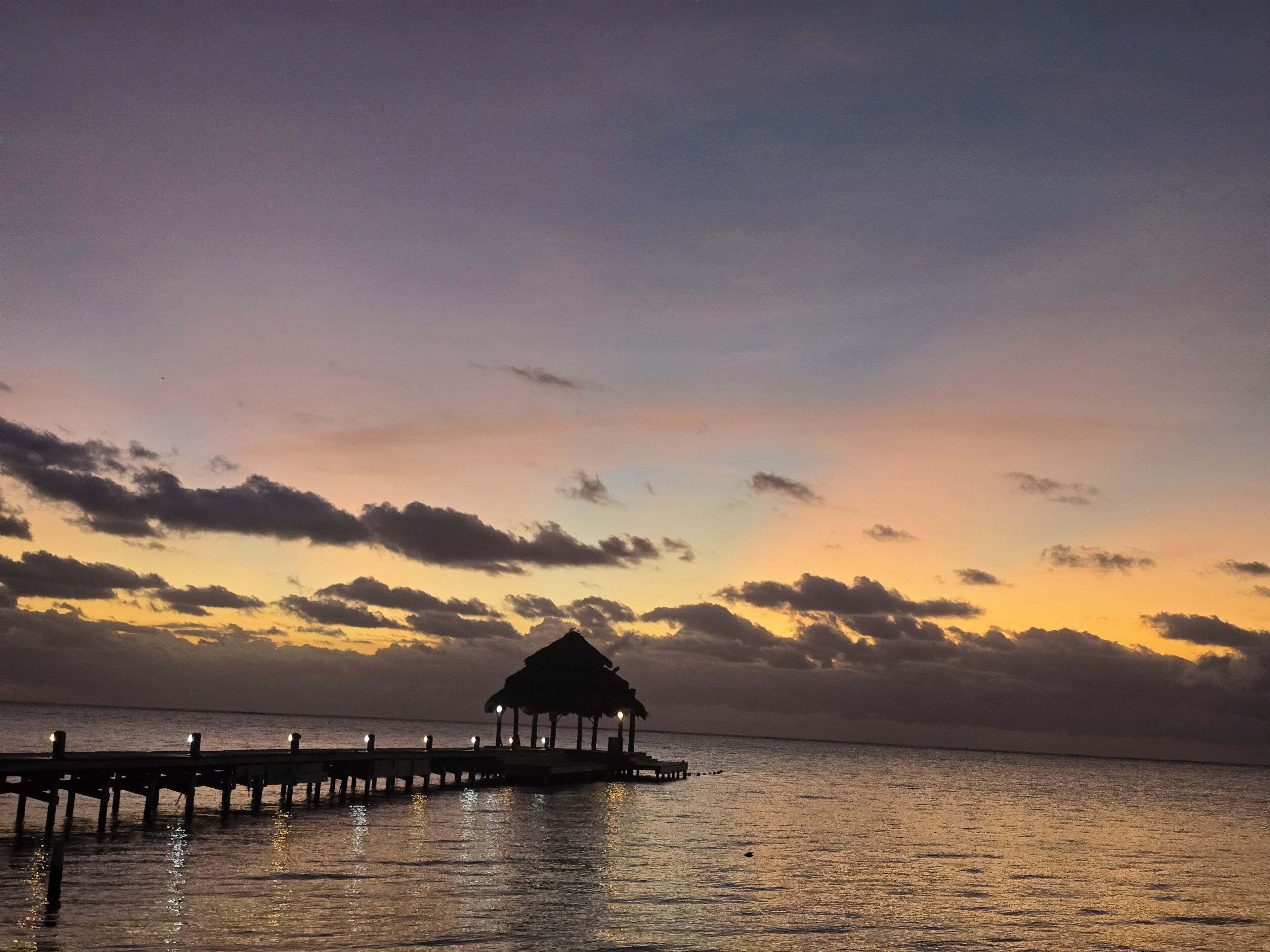 A pier extending into calm waters with a thatched-roof structure at the end.