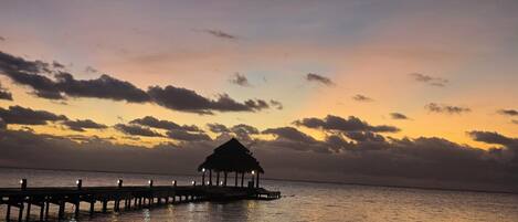 A pier extending into calm waters with a thatched-roof structure at the end.