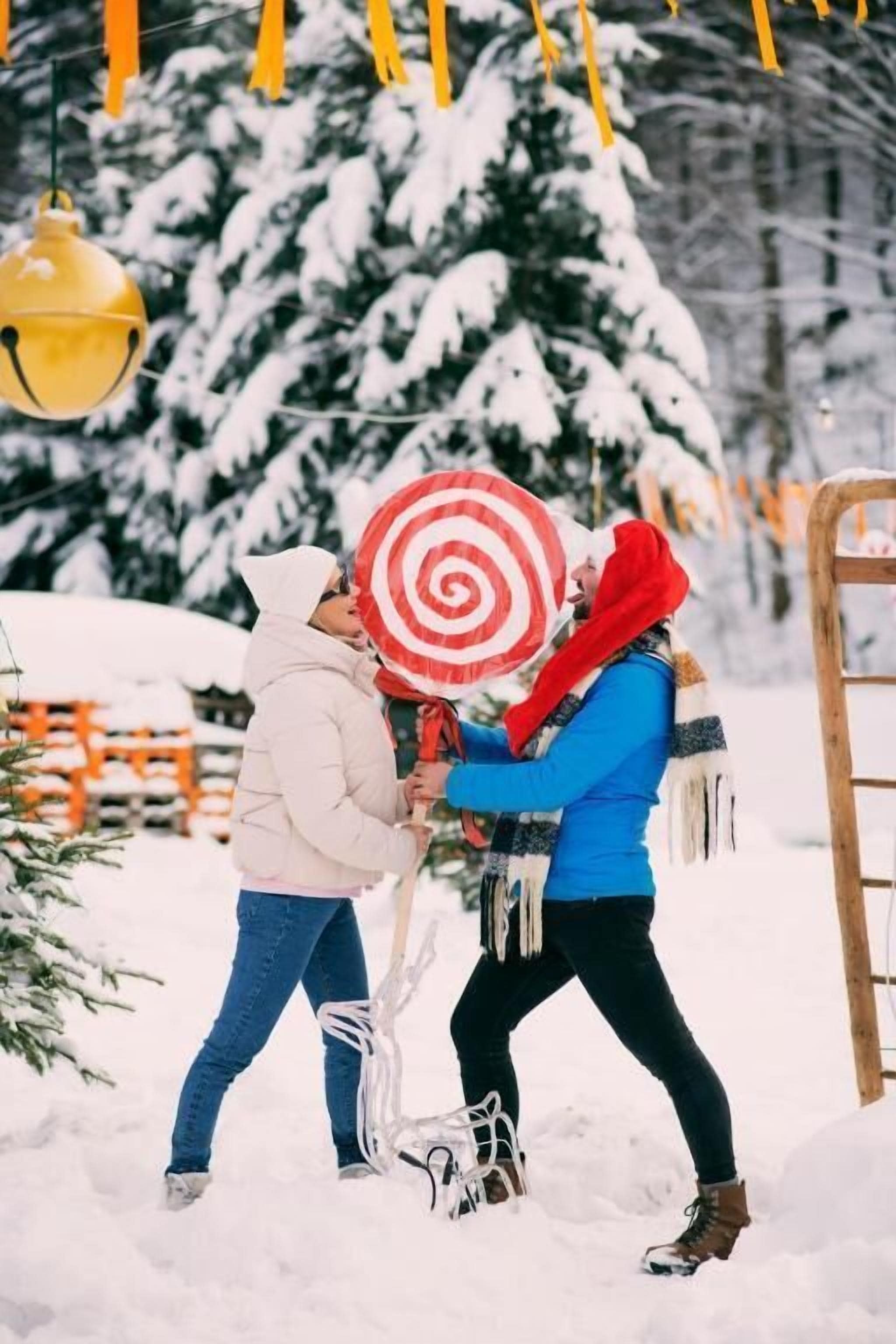 Two people in a snowy outdoor setting with a Christmas tree and decorations.