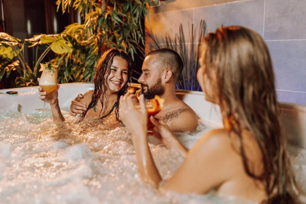 Three people in a hot tub with bubbles, surrounded by plants.
