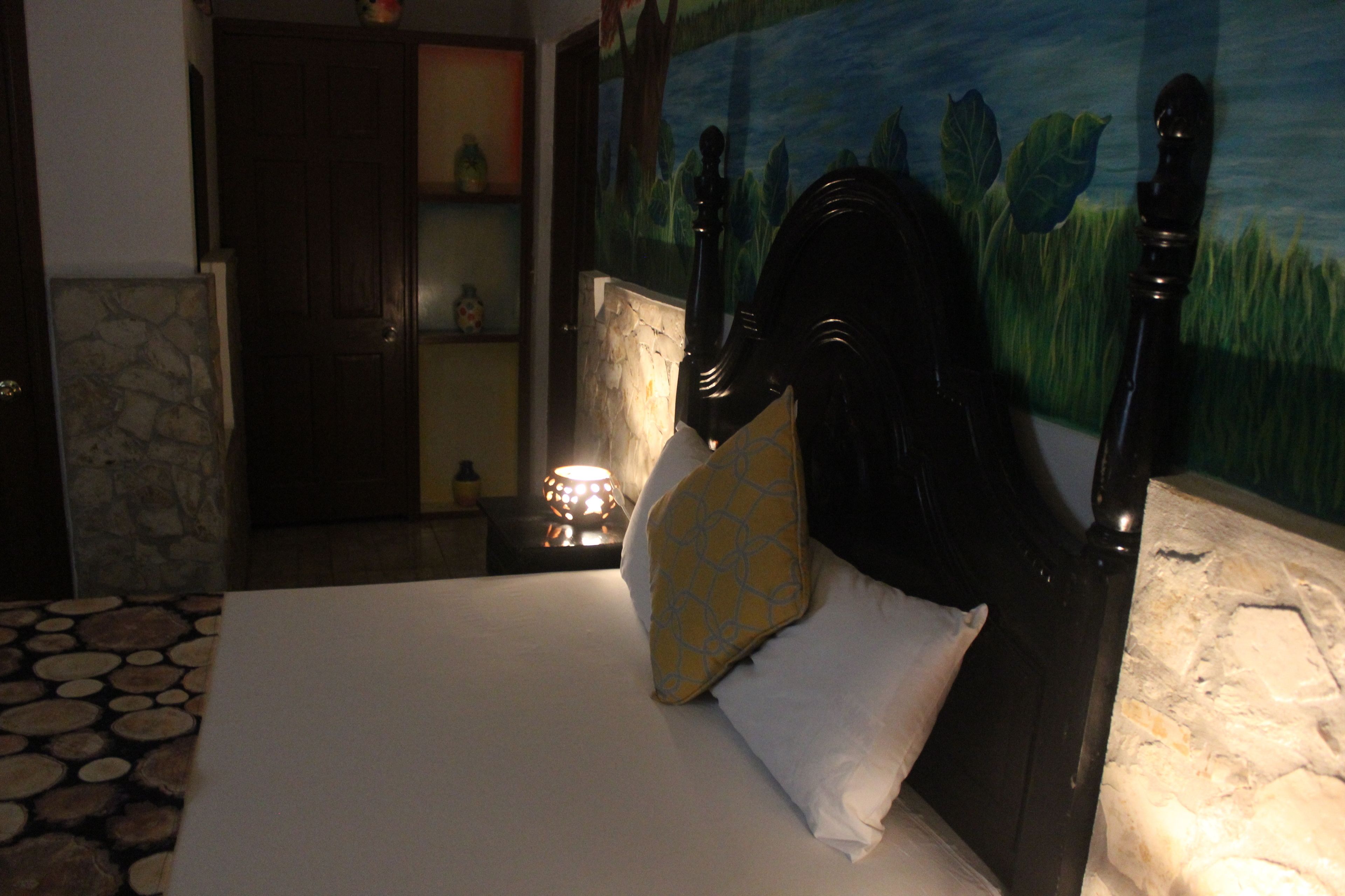 Quarto com uma cama, mesa de cabeceira, abajur e parede de pedra.