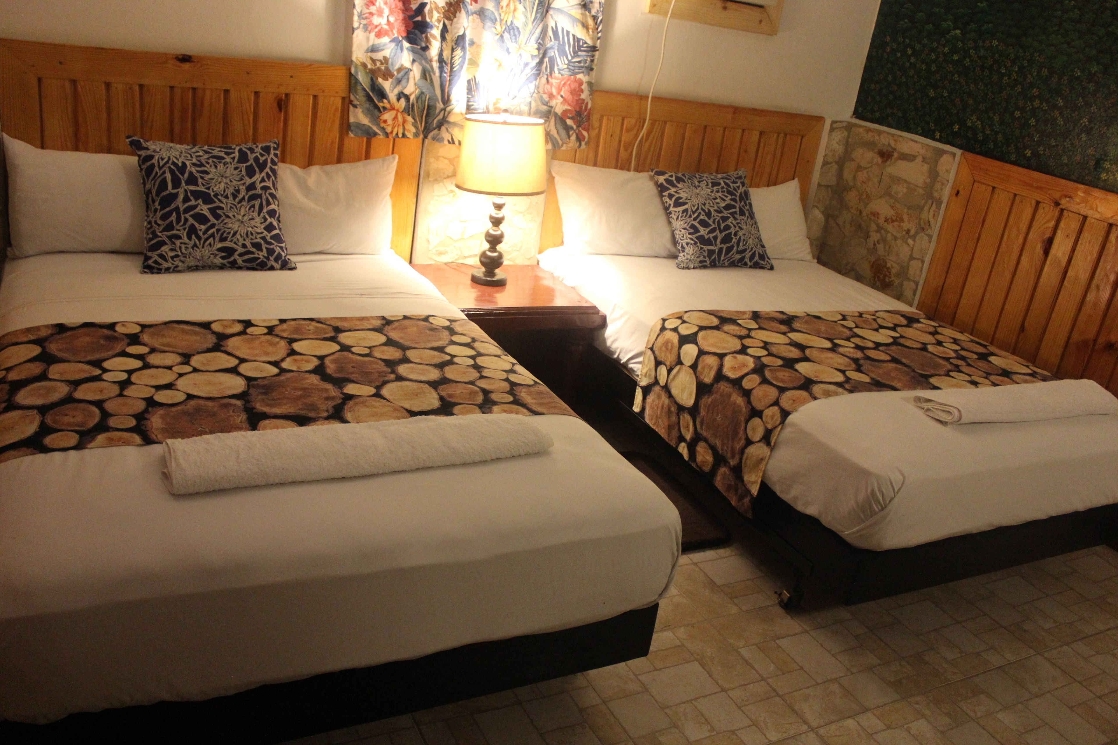 A hotel room with two beds, each with a patterned bedspread, a wooden headboard, and a nightstand with a lamp.