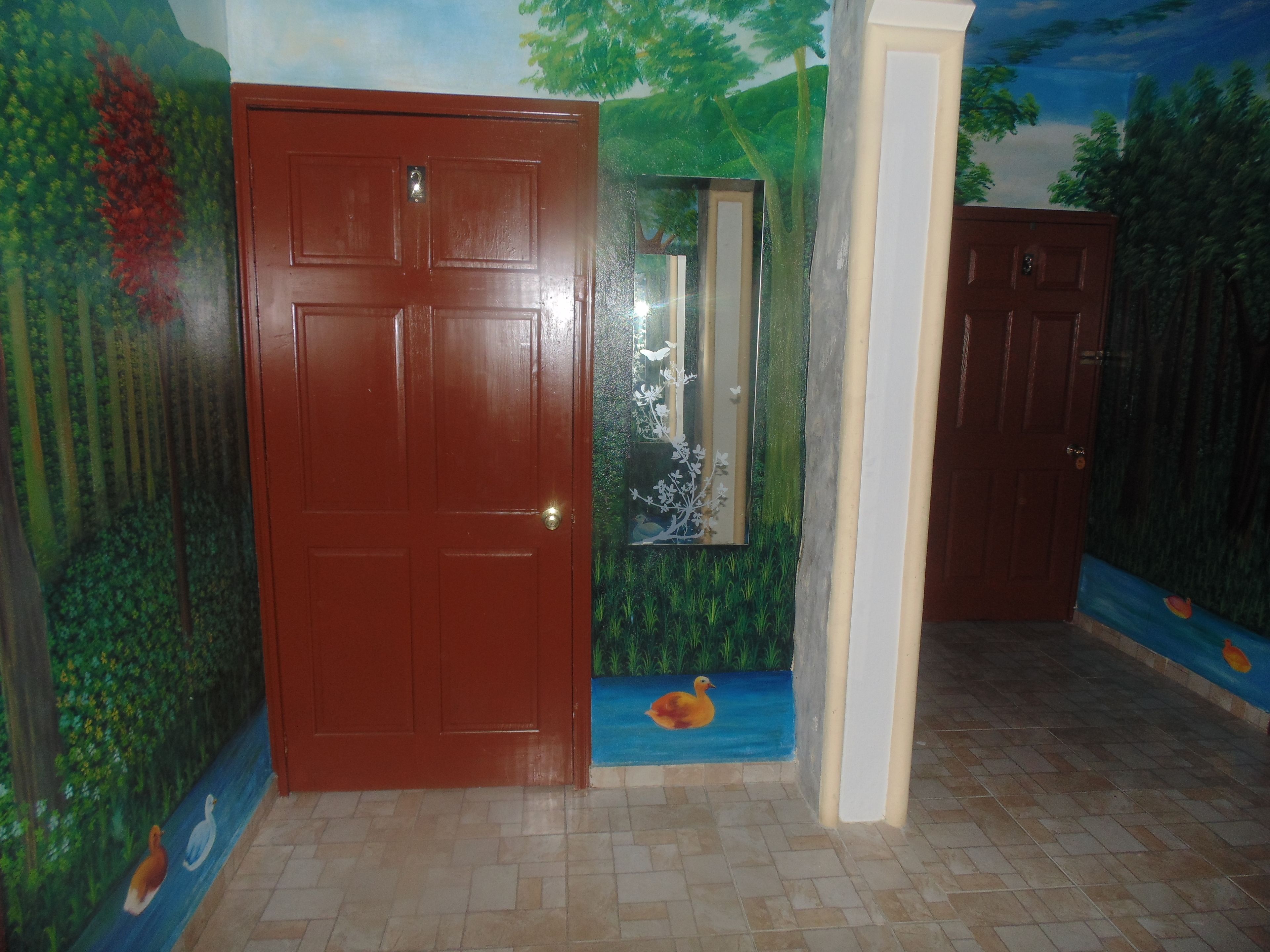 A room with a wooden door, a mirror, and a mural depicting a forest scene with birds and a duck.