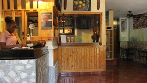 A reception area with a wooden counter, stone wall, and tiled floor. - Metro Residences Hotel (Cap-Haitien)