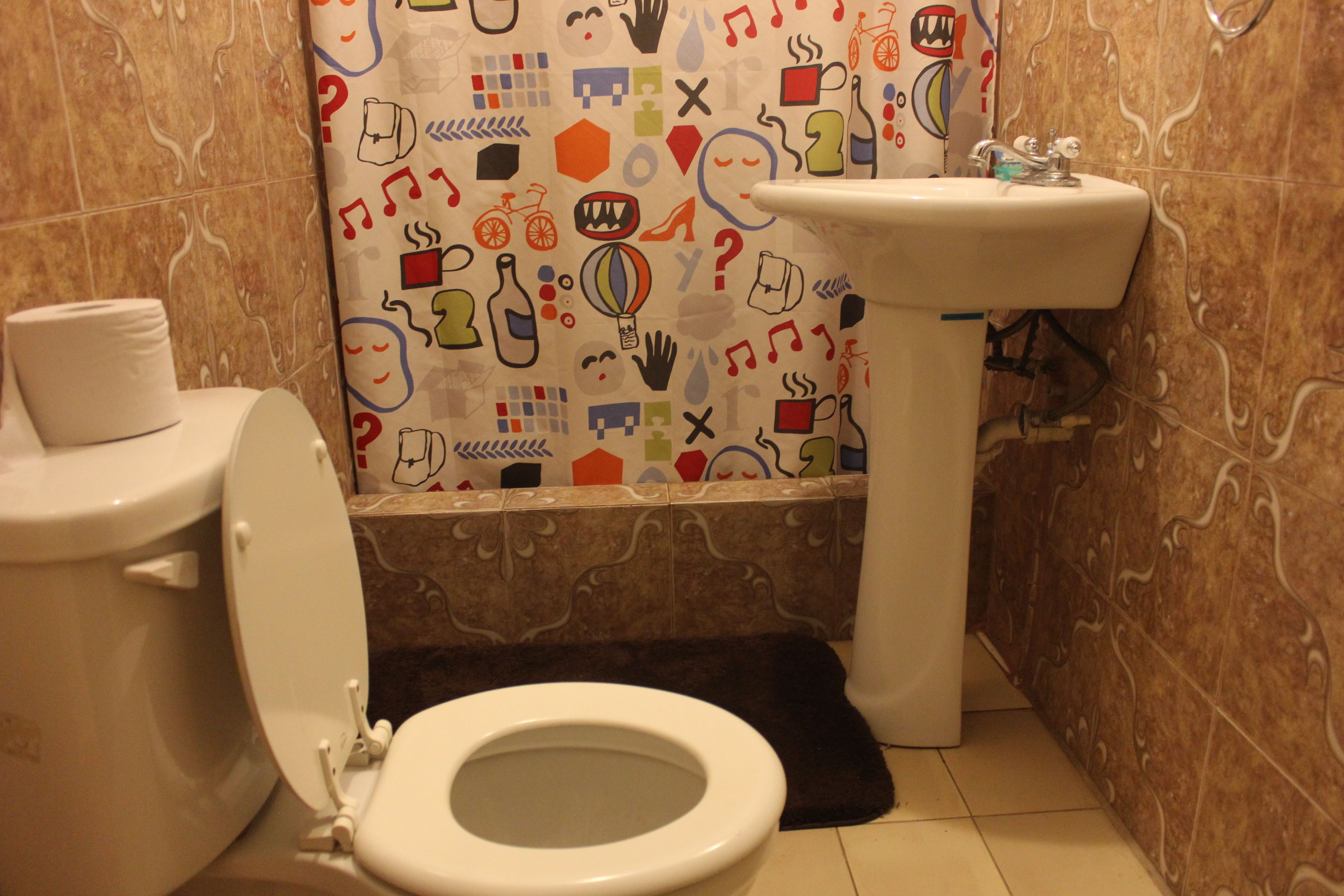 Un baño con inodoro, lavabo y cortina de ducha estampada.
