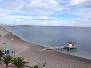 Una playa con un muelle que se adentra en el agua, arena dorada y cielo despejado.