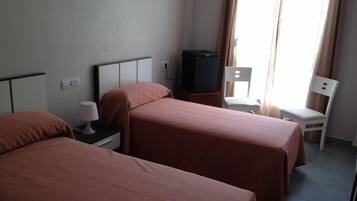 Una habitación de hotel con dos camas, un televisor sobre un mueble bajo, una silla y una lámpara.