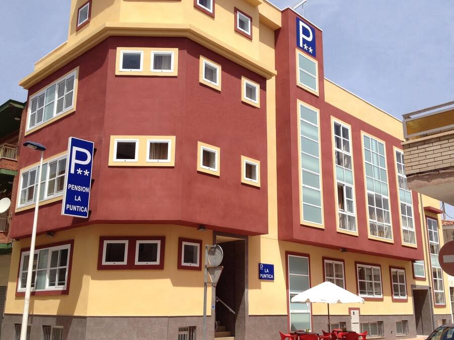 Un edificio de varios pisos con fachada amarilla y detalles en rojo, con varios letreros de estacionamiento y una escalera que conduce a la entrada.
