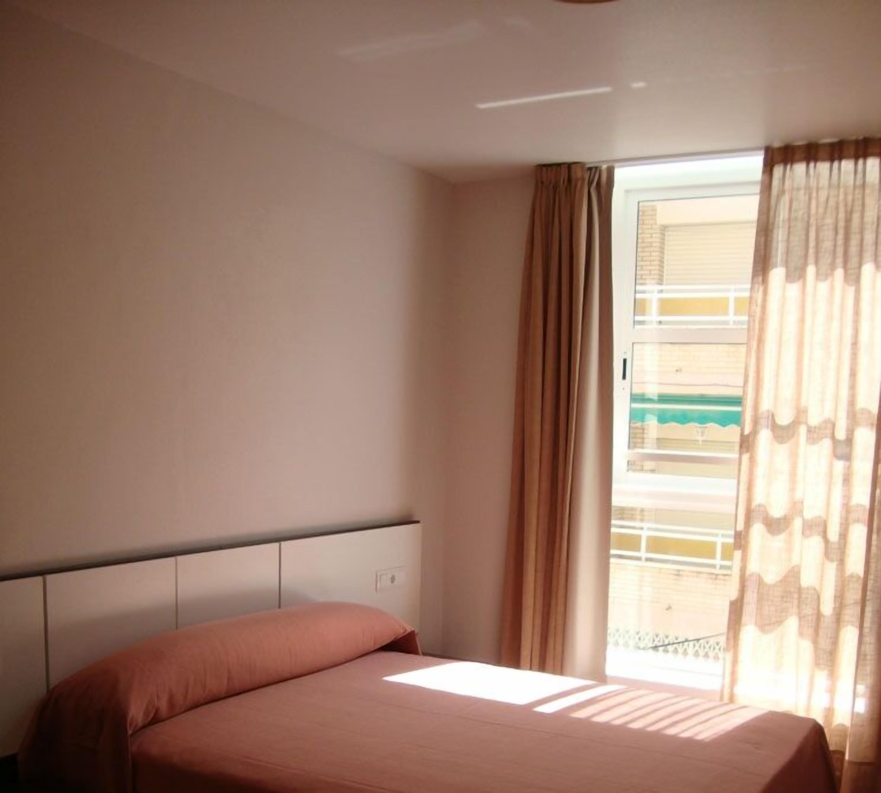 Un dormitorio con cama, cabecera y ventana con cortinas.