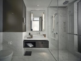Une salle de bain moderne dotée d’une douche en verre, d’un lavabo blanc avec un meuble-vasque en bois et d’un sol carrelé en marbre.