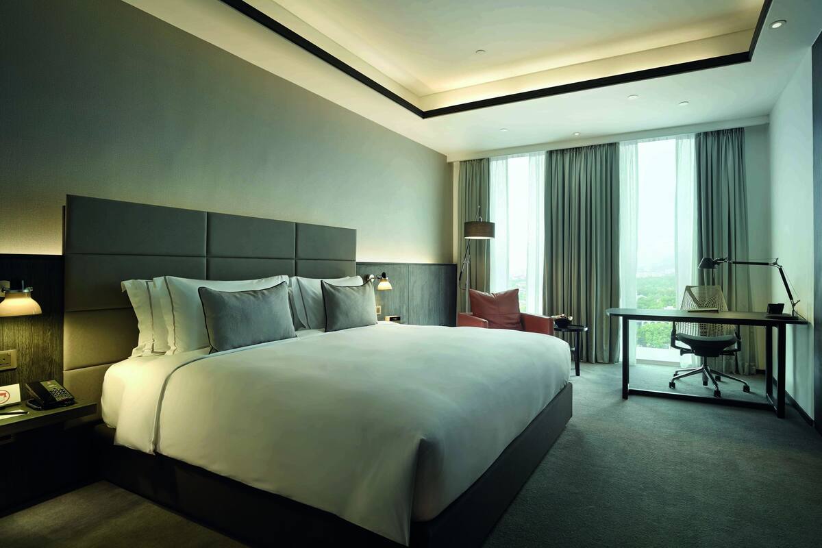 Una habitación de hotel moderna con una cama grande, un escritorio con silla, un televisor de pantalla plana y vistas a la ciudad a través de la ventana.