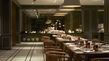 A long dining table set with chairs, overhead pendant lighting, and a tiled floor.