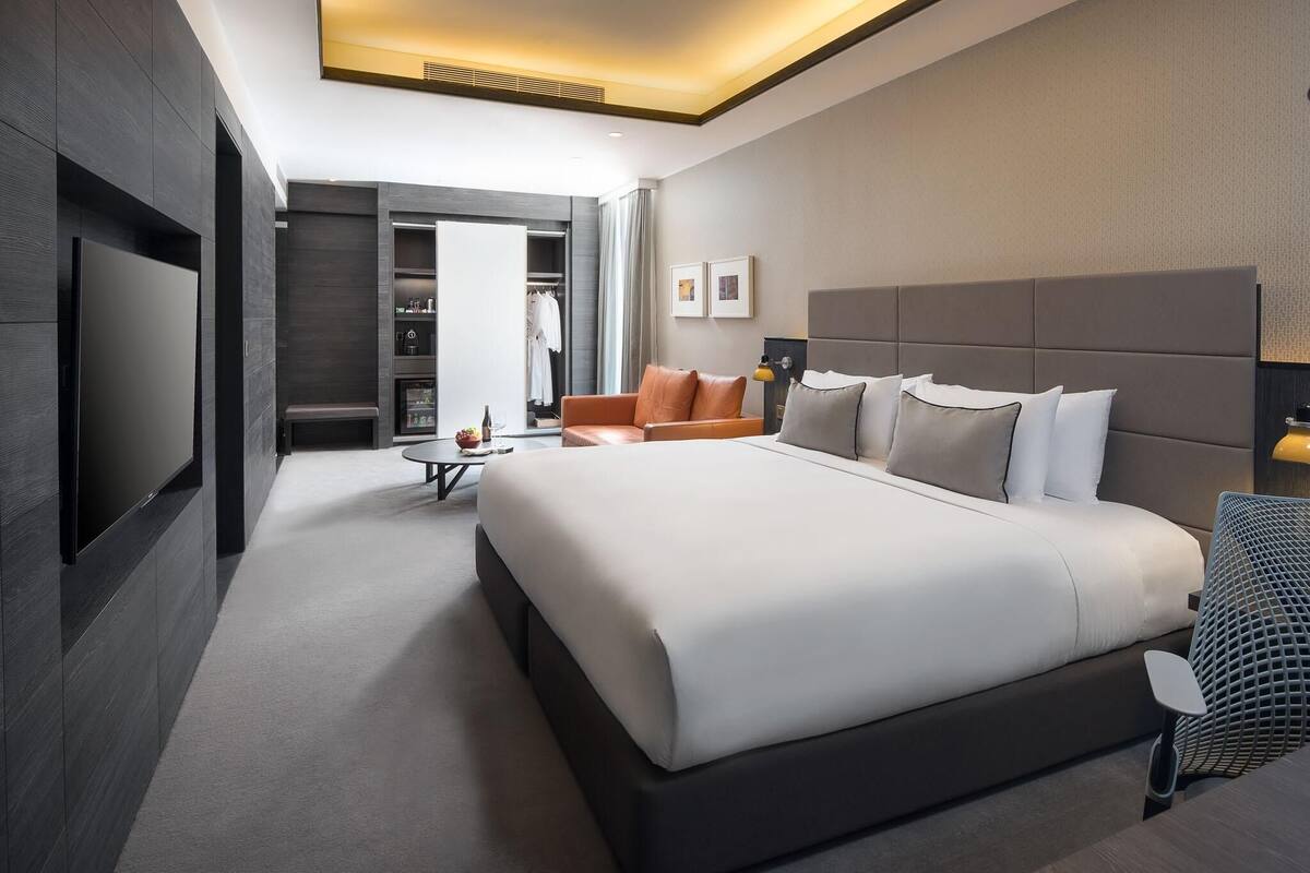 Una habitación de hotel moderna con una cama grande, zona de estar, armario y televisor.