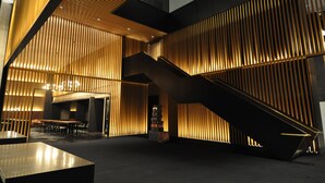 A modern interior with a staircase, wooden slats, and a reception area with tables and chairs. - G Hotel Kelawai (George Town)