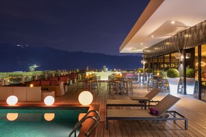 A rooftop bar with a pool, lounge chairs, and tables.