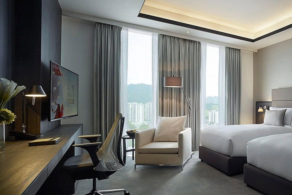 A hotel room with a bed, desk, chair, and a view of the city.