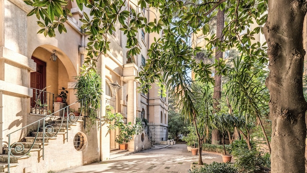 A courtyard with a stone staircase leading to an entrance, surrounded by potted plants and trees. - Gardenia Suite (Rome)