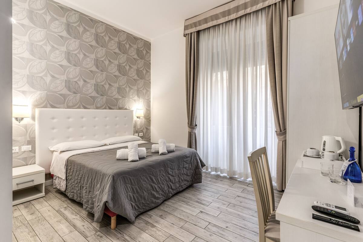 A hotel room with a large bed, a desk with a TV, and a window with curtains.