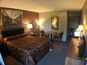 Habitación de hotel con una cama grande, un escritorio, dos sillas, un espejo y un cuadro en la pared.