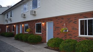 Une rangée de chambres de motel aux murs recouverts de bardage blanc et agrémentées d’éléments en brique, chacune dotée d’une petite fenêtre et d’une porte.