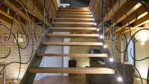 Una escalera de madera con barandales de metal que conduce a una habitación con pared de ladrillo y una cama.