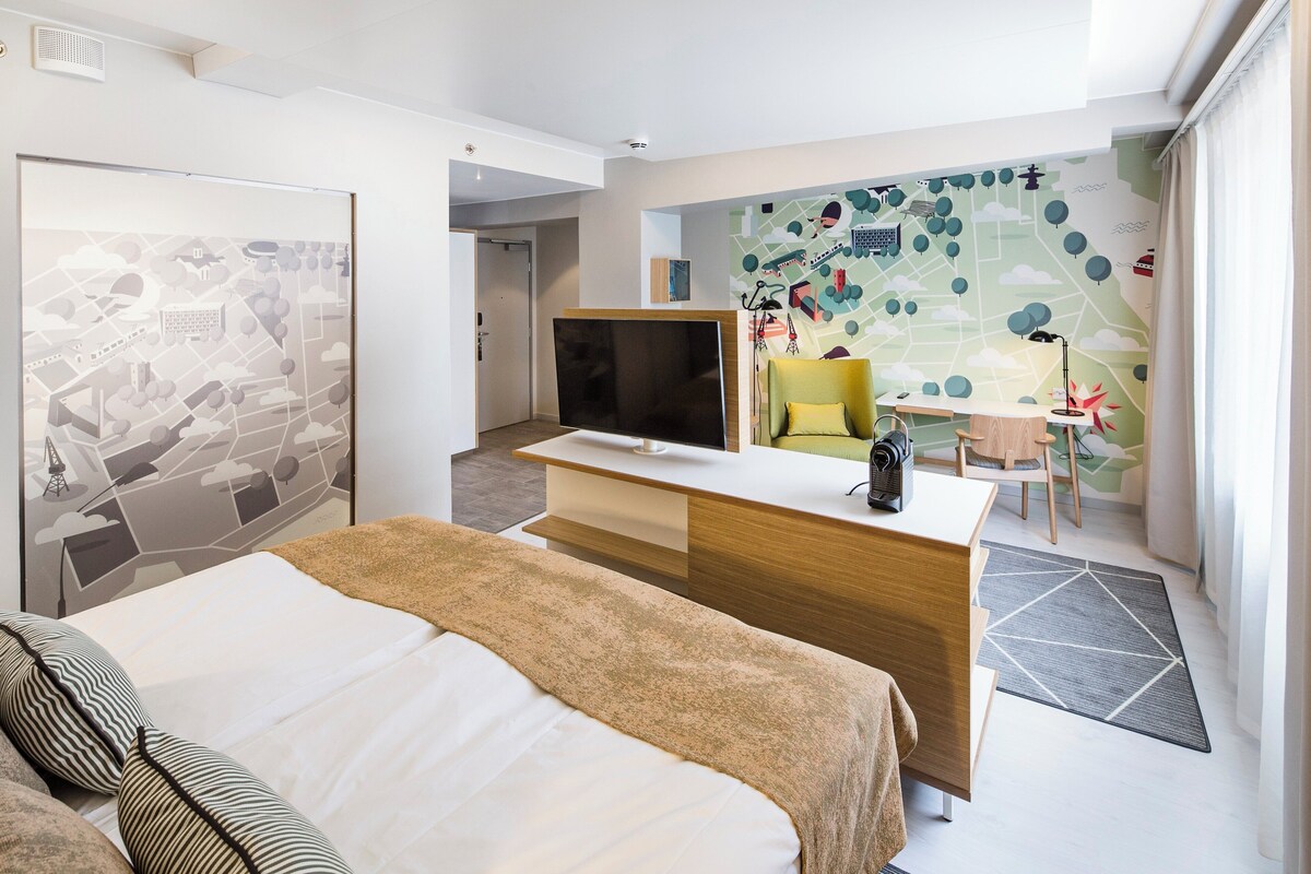 Ein Hotelzimmer mit einem Bett, einem Schreibtisch, einem Fernseher, einem Sessel und einer Wand mit Weltkarten-Motiv.