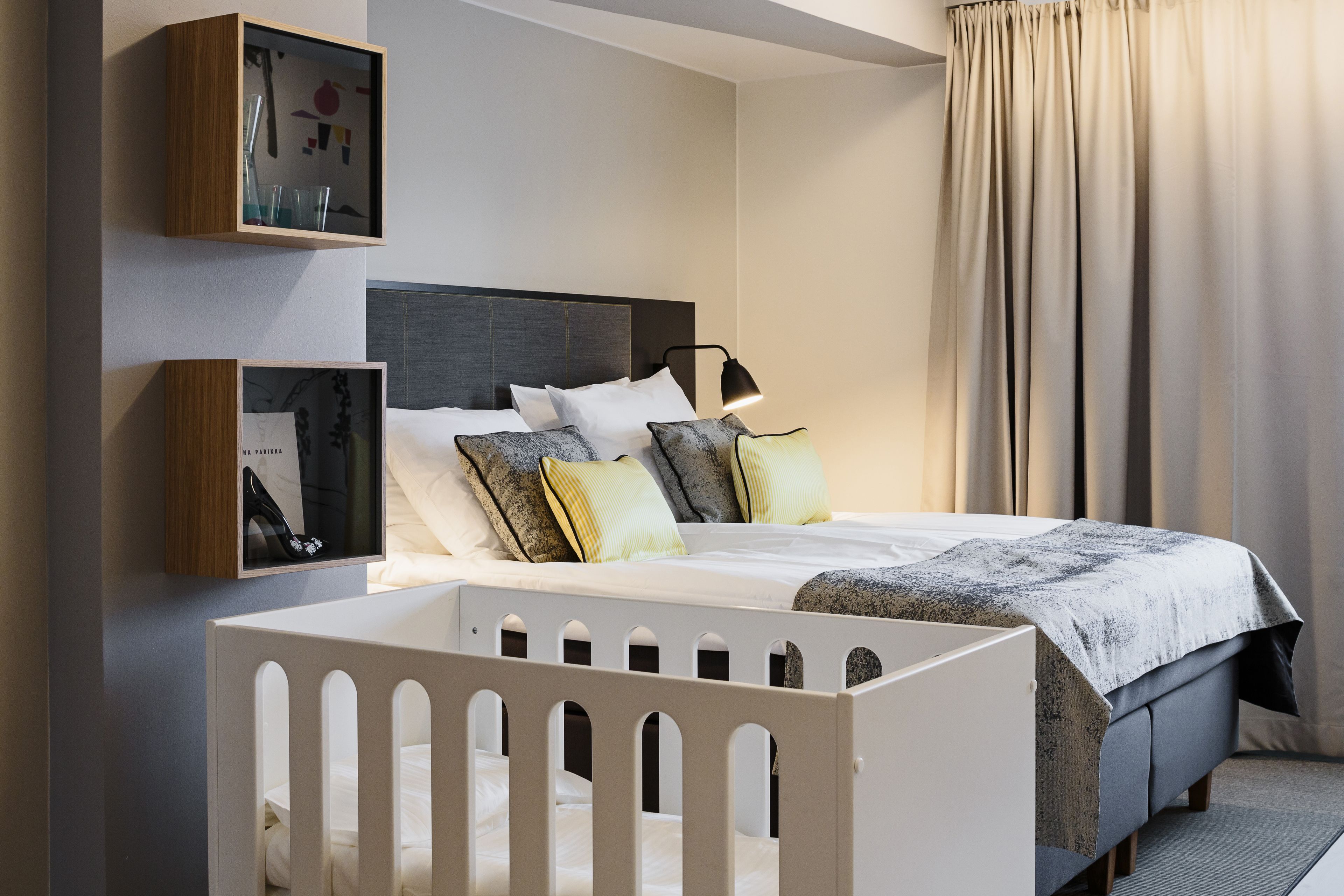 A modern bedroom with a large bed, a crib, and a bedside table with a lamp.