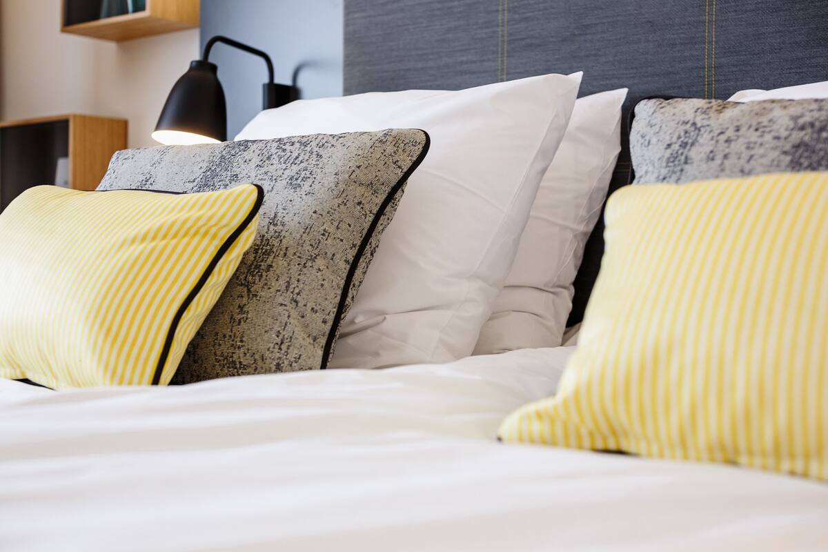 A neatly made bed with white and striped pillows, a headboard, and a bedside lamp.