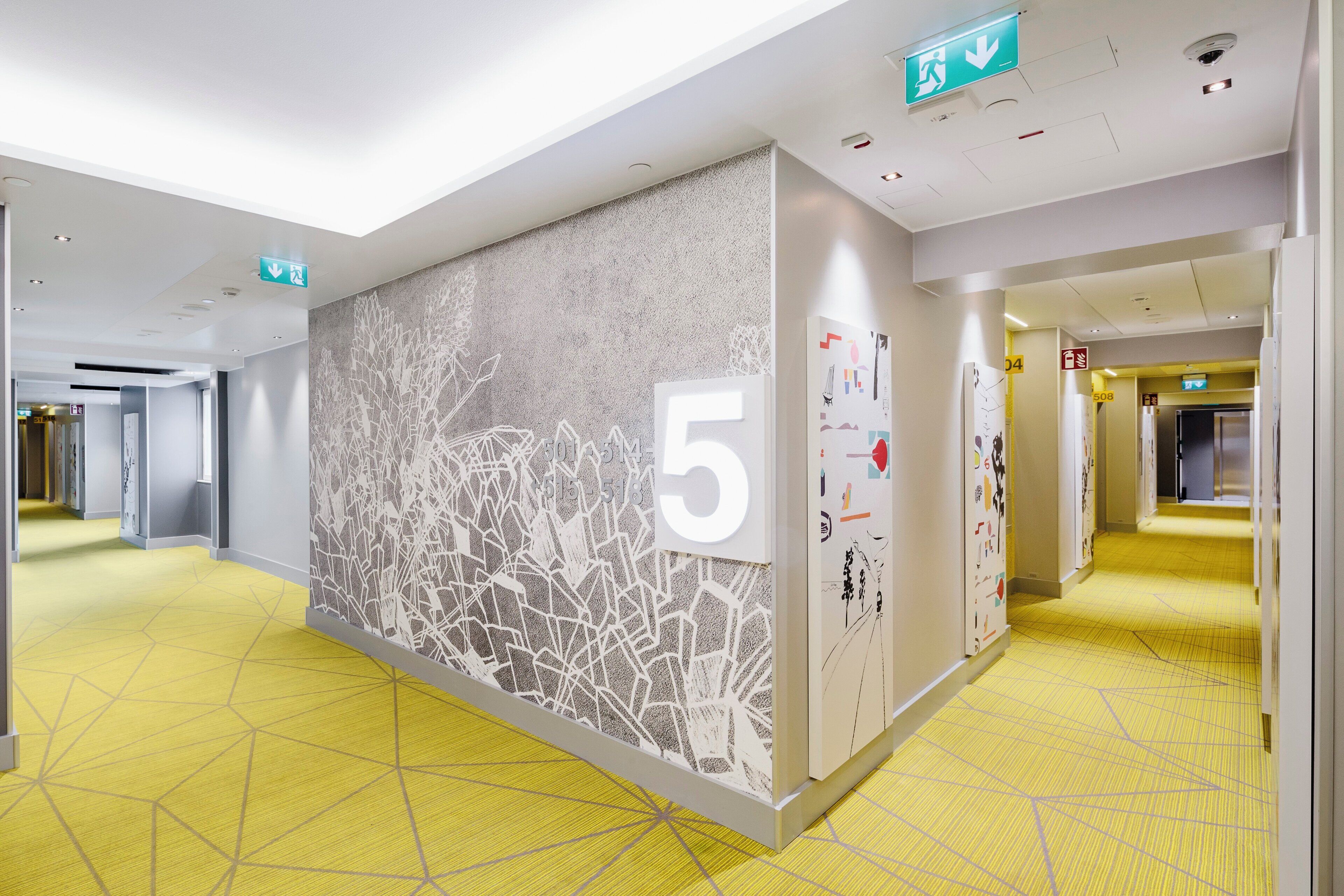 Een hotelgangen met een nummer 5 bord, tekens voor een nooduitgang en een patroon op de muur.