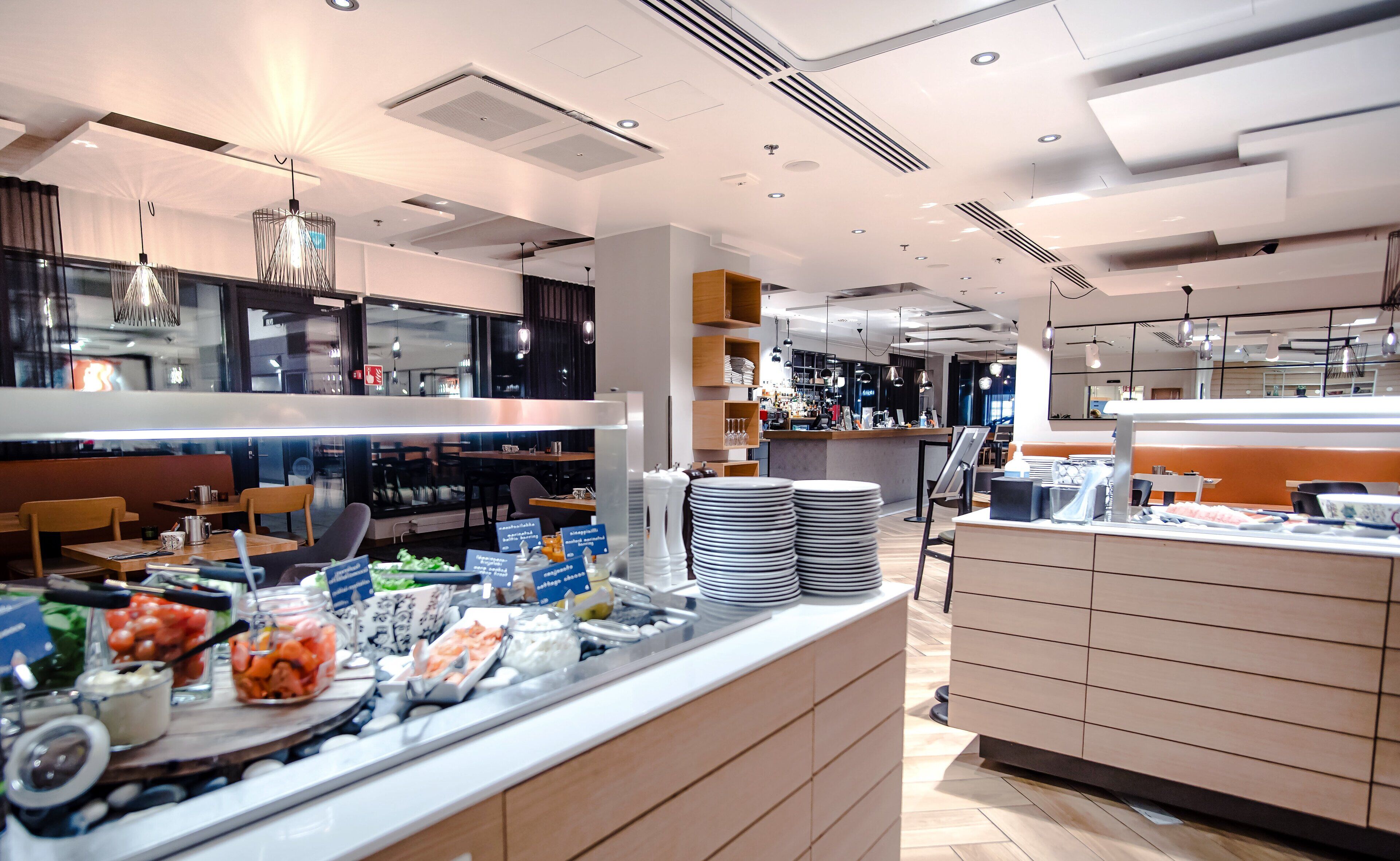 A modern restaurant with a buffet setup, including various food items and a counter with stacked plates.